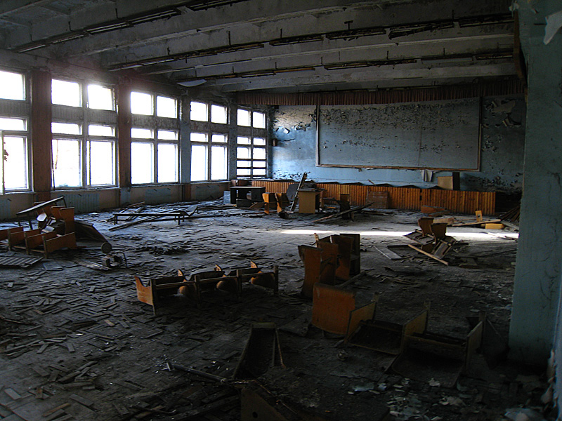 A large classroom, empty except for old desks and chairs, or what's left of them.